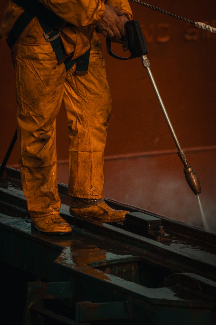 journey-02 A worker in yellow safety gear uses a pressure washer on industrial equipment.