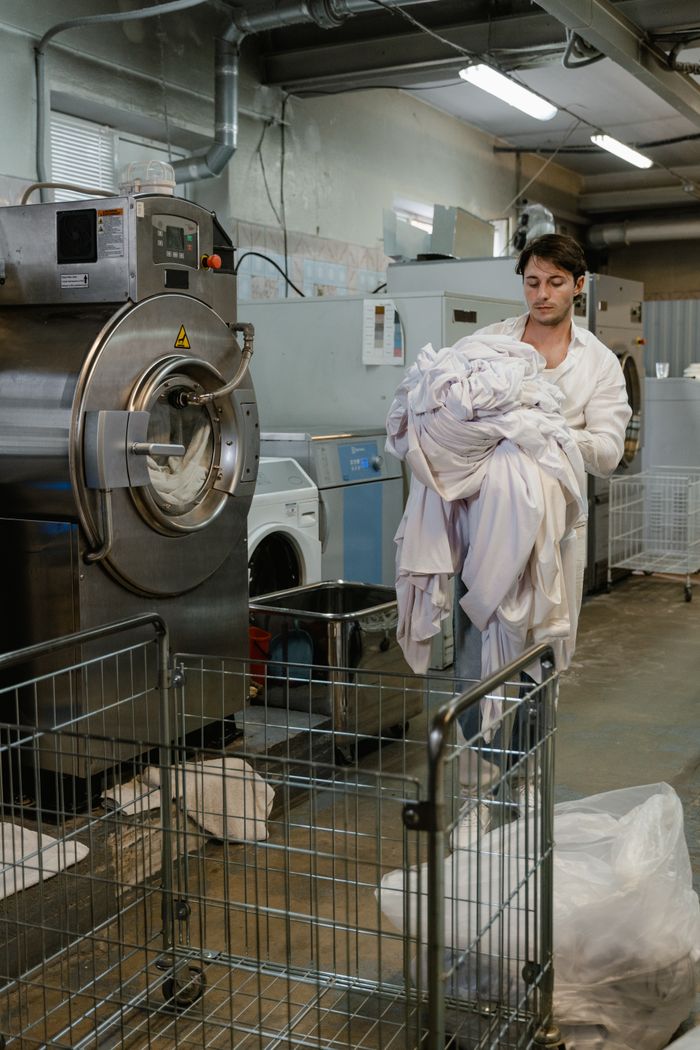 services-img A man carries a large load of laundry in a commercial laundry facility.